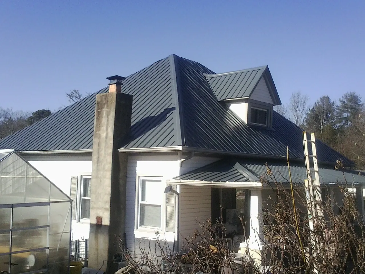 Dark blue standing seam metal roof on a white farmhouse with dormer — Slate & Tile Roof Repair by Roofing Brothers in Avilla