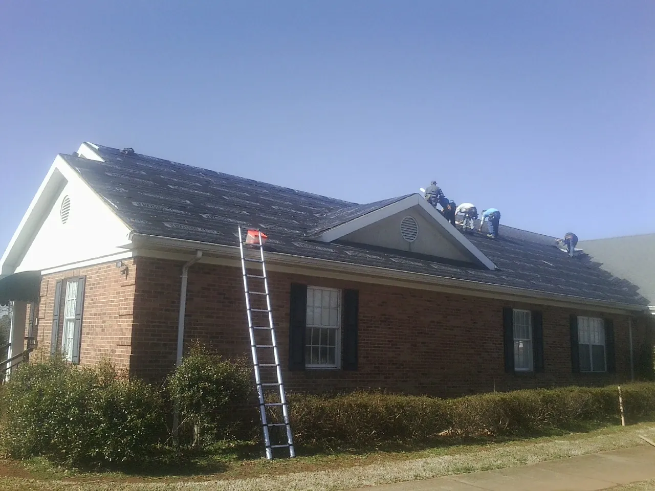 Crew tearing shingles off a brick ranch roof with a ladder set — Emergency Roof Repair work by our crew in Avilla