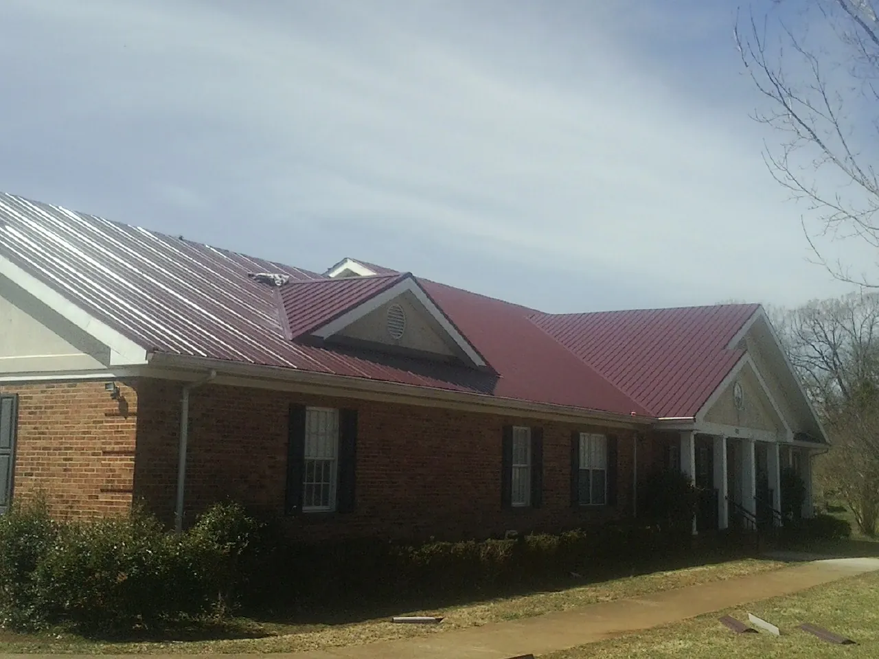 Red metal roof with gabled entries on a long brick building, from a Hail Damage Roof Repair job in Avilla