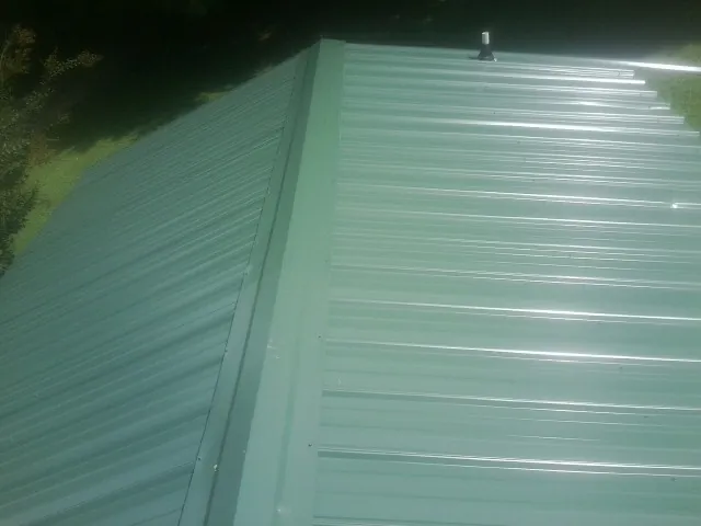 New green metal panels meeting at the ridge of a roof — Flat Roof Repair work by our crew in Avilla