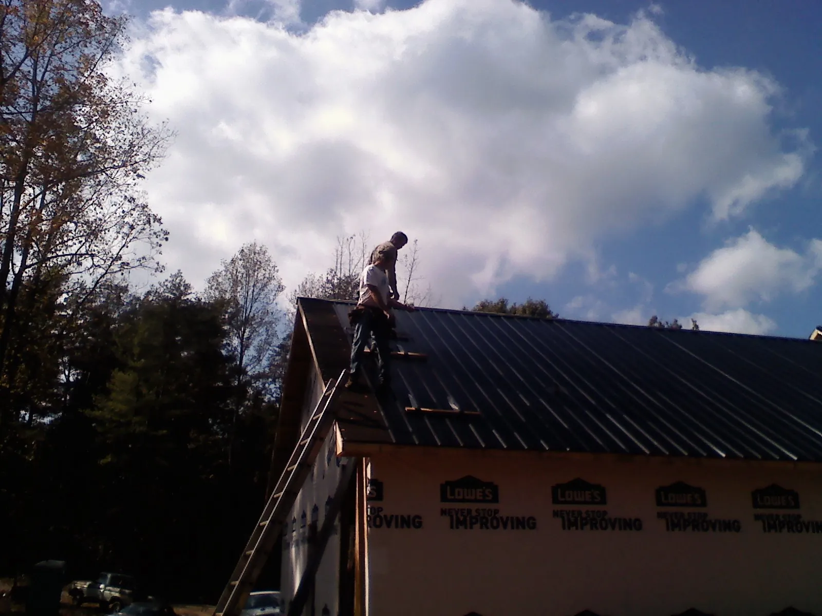 Roofer fastening dark metal panels high against a cloudy sky, from a Roof Inspection job in Avilla