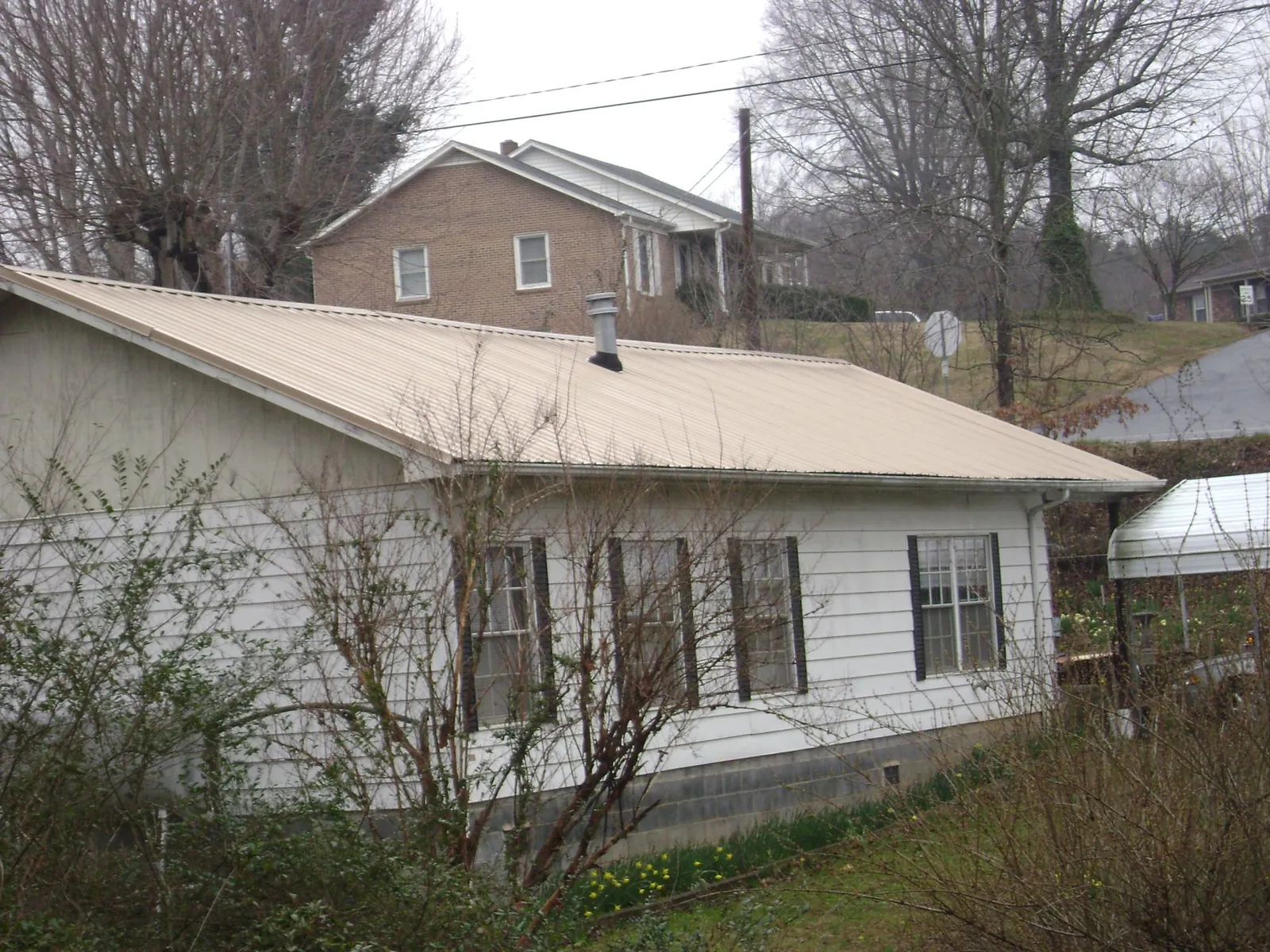 Tan metal roof on a white sided house set into a hillside — Commercial Roofing by Roofing Brothers in Avilla